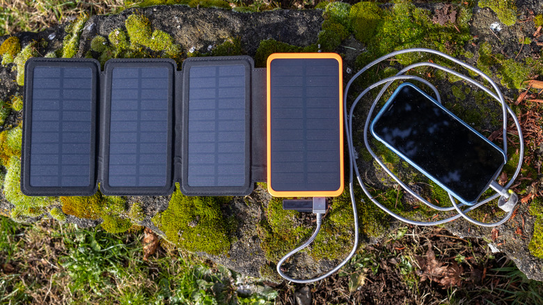 A portable solar charger panel charging a phone outdoors