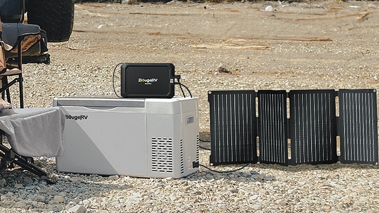 A car fridge placed on a rugged terrain along with four solar panels.