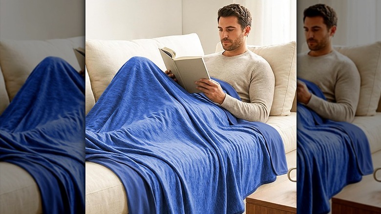 Man reading a book on a sofa with a cooling blanket on him.