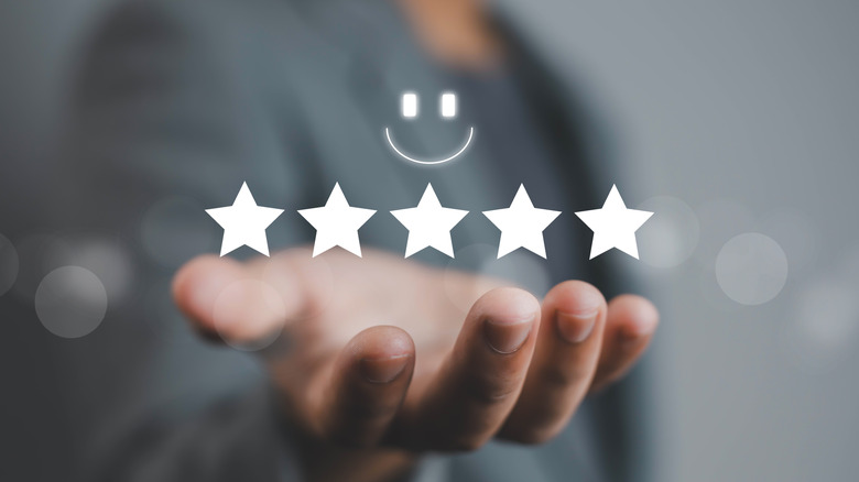 Holographic image of five stars and a smiley emoji above a hand.