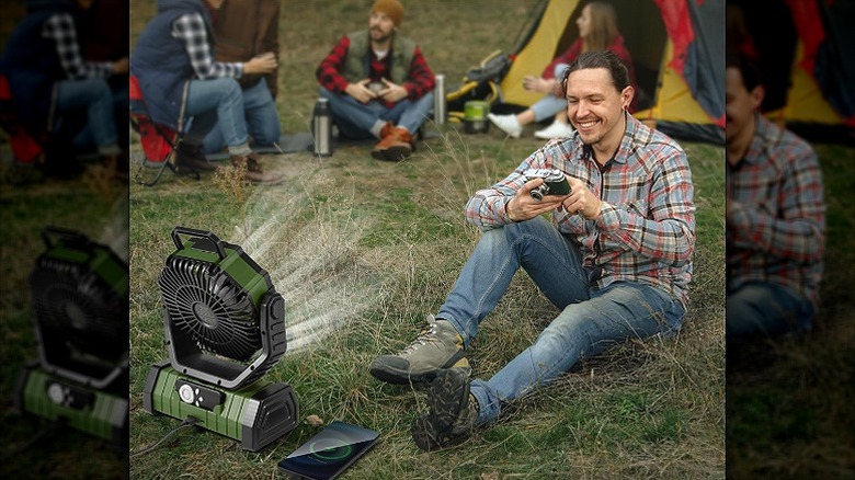 A man enjoying cool breeze from a portable camping fan at a campsite.