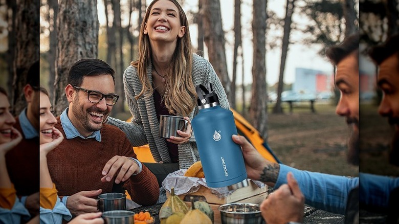 A family enjoying picnic outdoors with an insulated water bottle in hand.