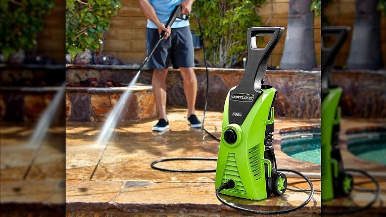 Washing floor with a green corded pressure washer.