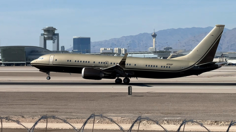 A matte silver-golden Boeing BBJ 737 Max 8 landing at Las Vegas, with the tail number N702F.