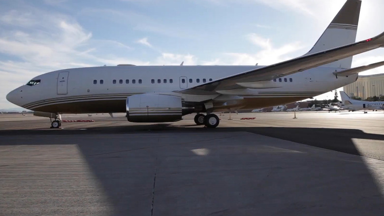 A golden and white Boeing BBJ1 from 2001 parked in a designated spot at a small regional airport.