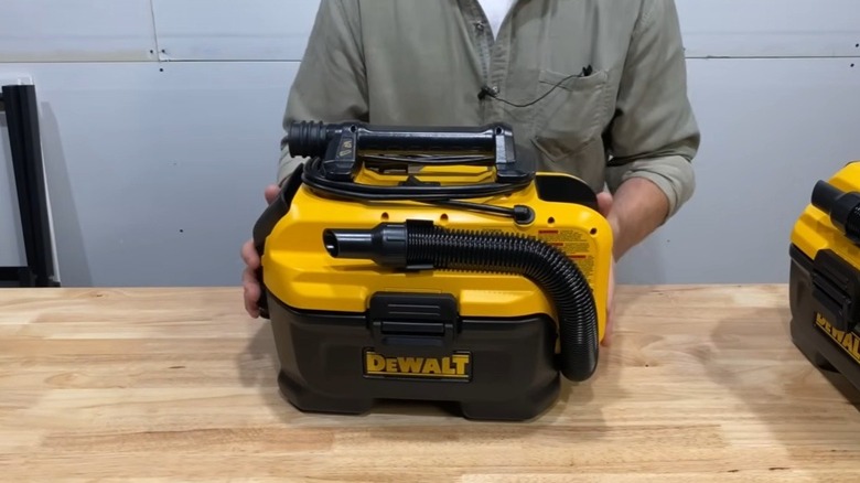 A person standing behind DeWalt shop vacuum on a desk.