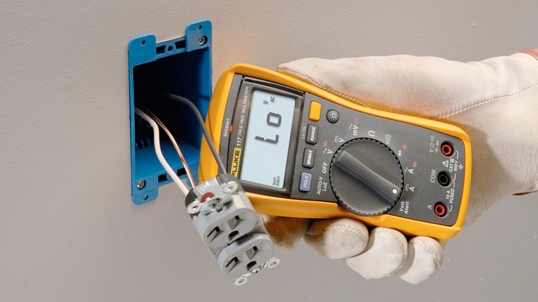 Person using Fluke multimeter on disassembled power outlet.