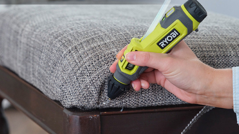 A person holding a Ryobi Glue Pen close to a piece of furniture.