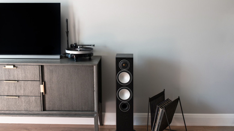 A speaker against a gray wall next to a television and a gramophone, both of which are placed on a TV unit
