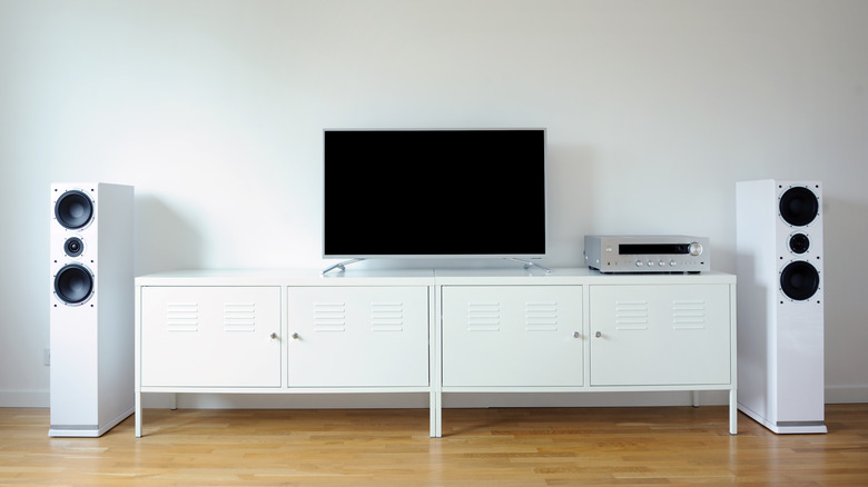 A television set up on a white TV unit with tower speakers on either side of it