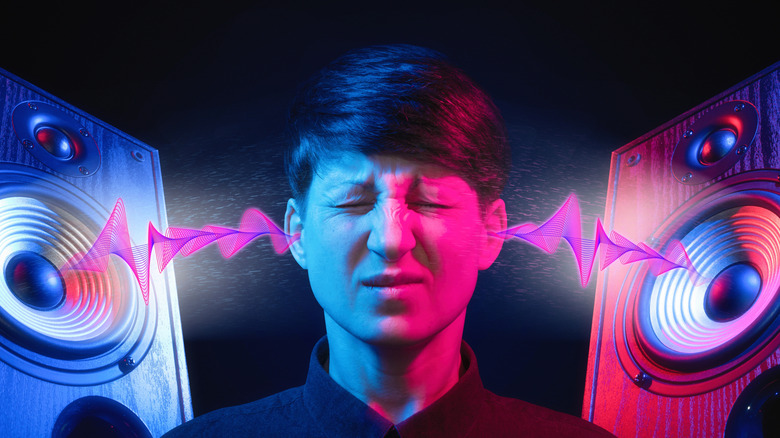 A person with an uncomfortable expression as two speakers blare into their eyes