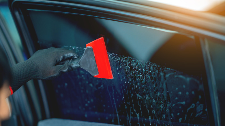 A professional detailing a car window with tint.
