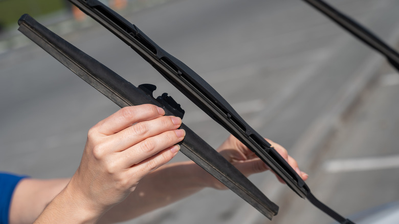 A person replacing windshield wipers on a car.