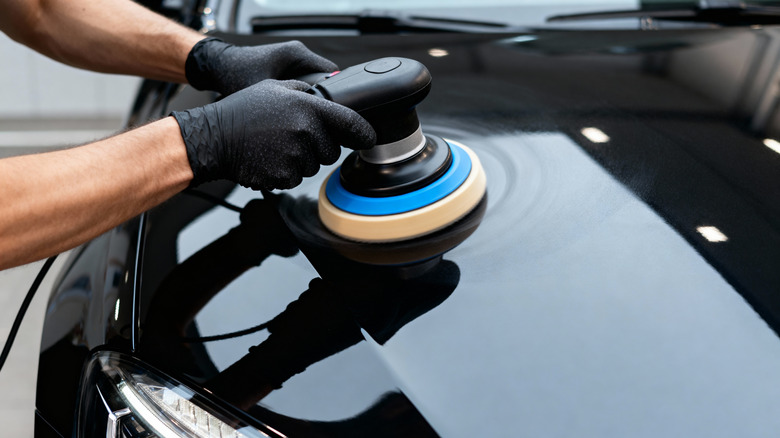 A person wearing gloves waxing a car with a power tool.