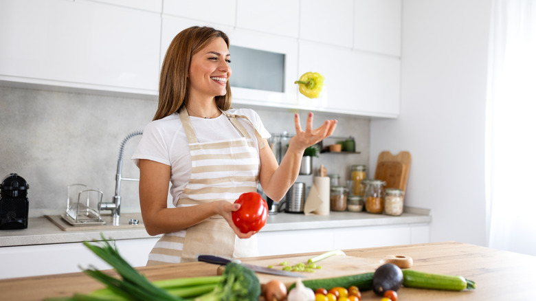Woman tossing yellow bell pepper in the air while standing behind a counter