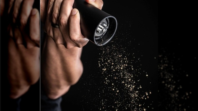 Hand on black background using a pepper grinder