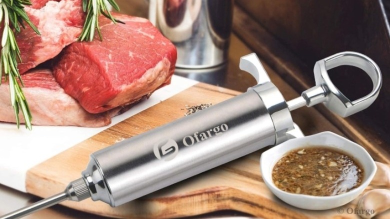 Meat injector on a cutting board alongside marinades and raw meat