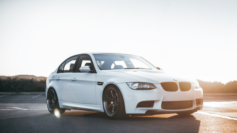White BMW M3 E90 on tarmac with sunset in background.