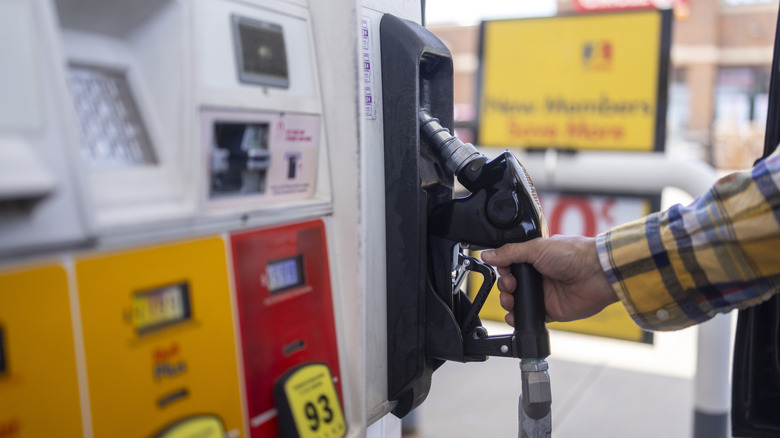 A hand in a plaid shirt holding a fuel nozzle refueling a car at a gas station pump