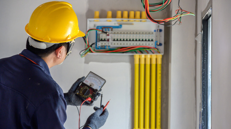 An electrician measuring voltage drop across an open electrical panel