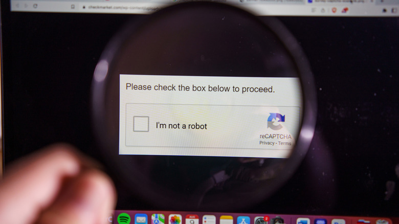 A hand holding a magnifying glass up to a screen displaying a reCAPTCHA verification tick box saying "I'm not a robot".