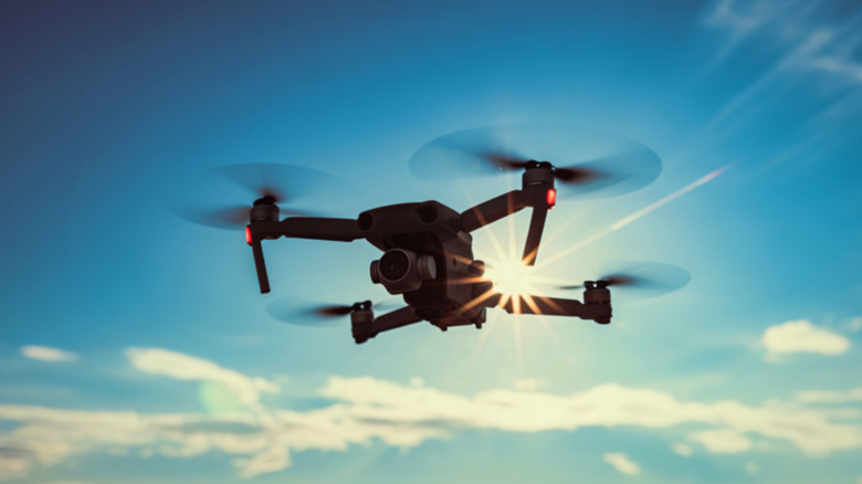 A dark silhouette of a drone against a bright blue sky