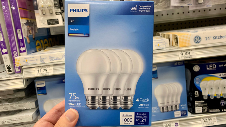 person holding a box of four Philips brand A19 light bulbs