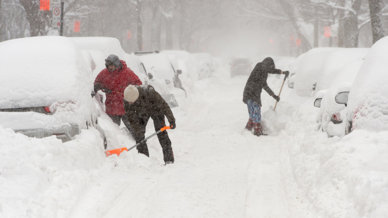 Three people in very snowy street shoveling cars out