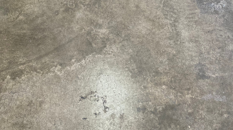 An old, worn concrete garage floor covered with cracks, scratches, and discoloration