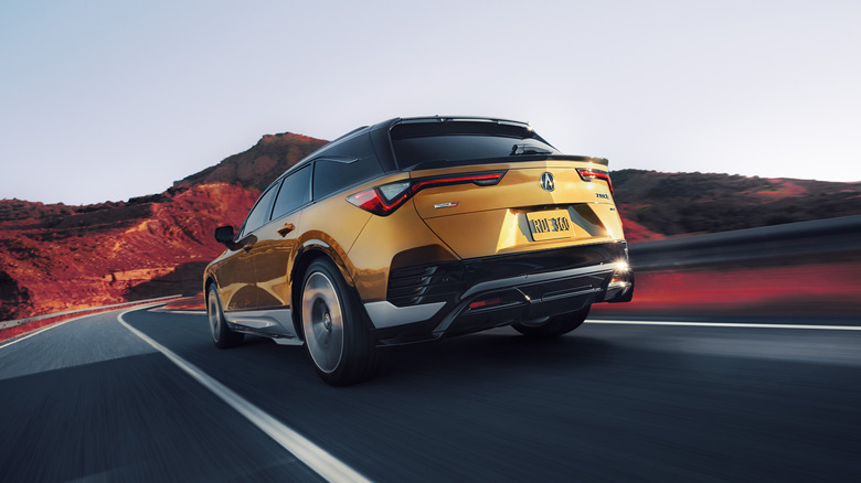 Rear 3/4 view of a gold Acura ZDX Type S on the move, desert road