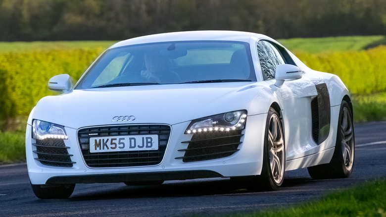 Un Audi R8 blanco conducido en la carretera con sus faros LED encendidos.