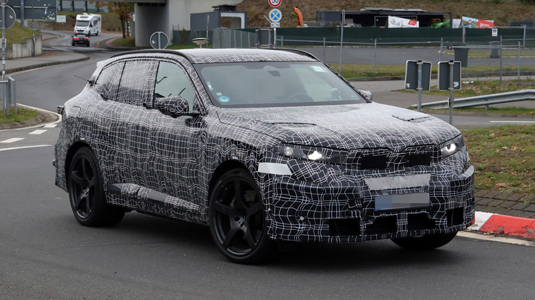 A BMW X5 M camouflaged car being driven on a public road.