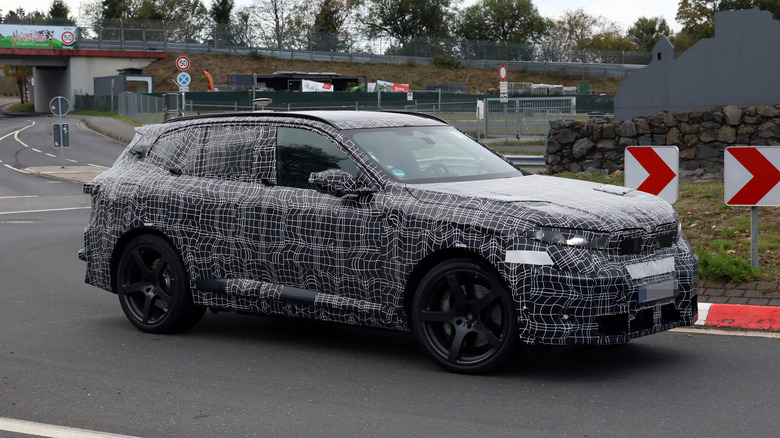 A camouflaged BMW X5 M being driven around a corner.