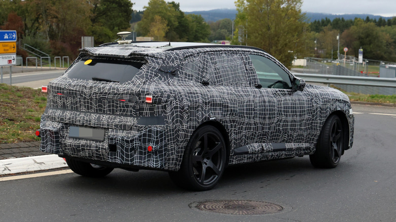 A camouflaged BMW X5 M driving on a public road.