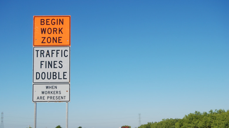Signs next to a highway indicating a work zone and doubled fines when workers are present