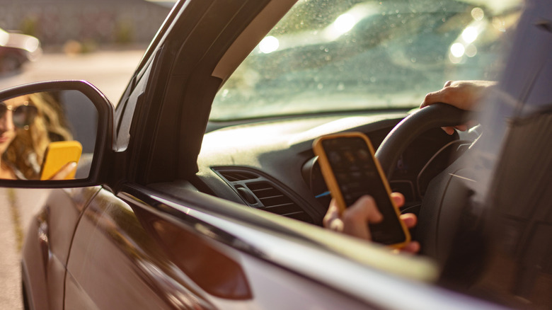 A view of a women behind the wheel of a car looking down at her cell phone