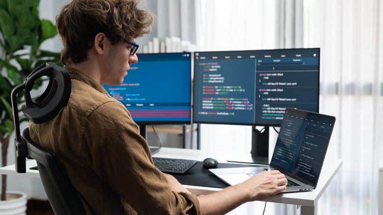 Software developer with laptop and multiple monitors
