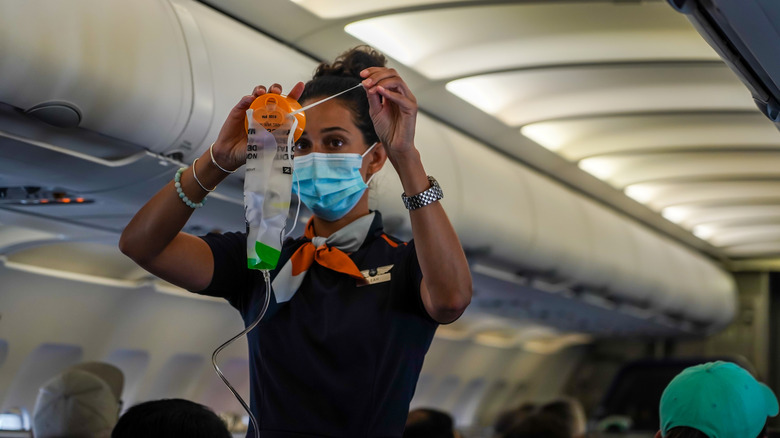 Cabin crew member demonstrating oxygen mask use.