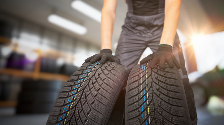 A car mechanic rolling two tires in a shop with sunshine in the background.