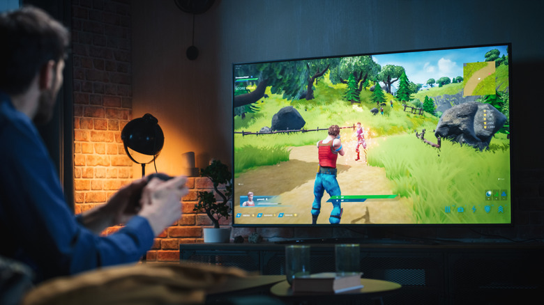A person playing Fortnite on a large television, brick wallpaper and spotlight in the corner