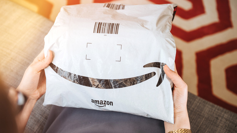 Women's hands holding an Amazon package with the woman's lap, a sofa and a patterned carpet in the background.