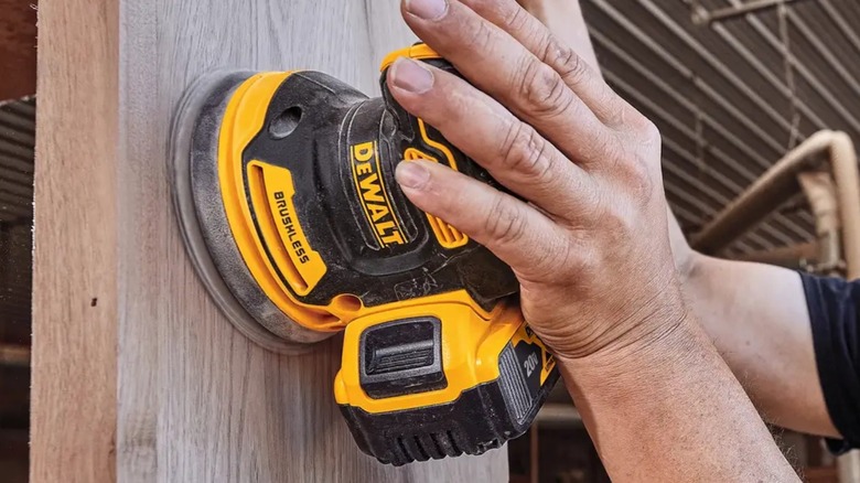 Person sanding wall stud with a DeWalt 20V Max Random Orbital Sander