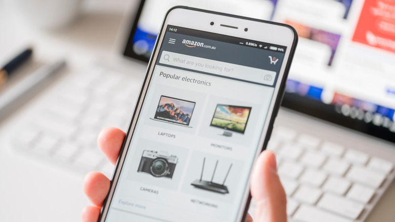 A hand holding a white smartphone with the Amazon shopping app open