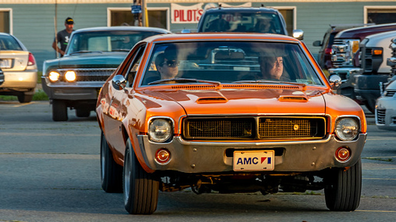The front of an orange AMC Javelin leaving a classic car show