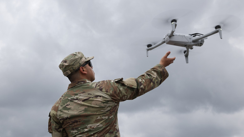 A soldier catching a drone against a gray cloudy sky.