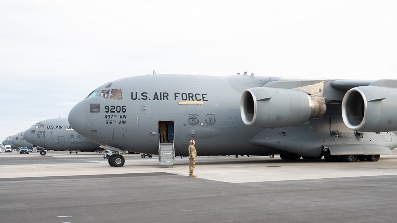 An Airman standing at attention beside a C-17 Globemaster on the tarmac of an airfield.