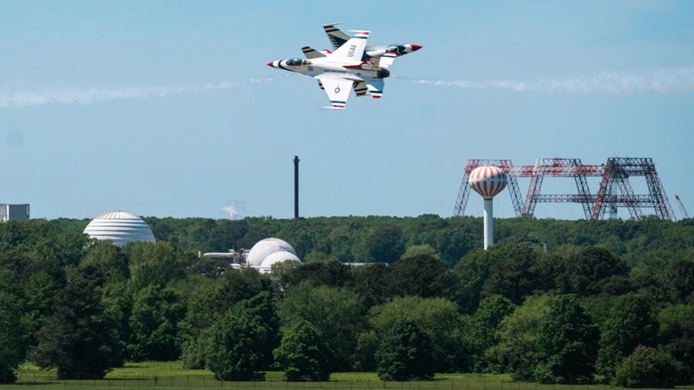 Two F-16s as part of the Thunderbirds stunt team fly by each other over greenery.