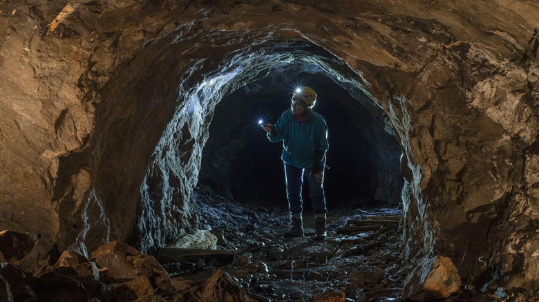 Geologist with a hard hat, headlight, and torch examining the walls of an abandoned mine shaft