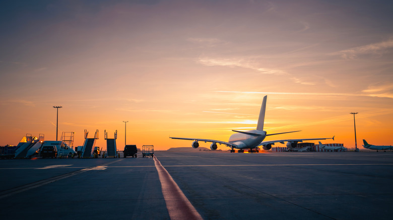 Wide shot of passenger airplane taking off from runway at sunset.