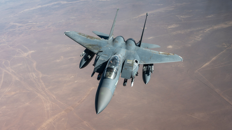 An F-15E Eagle flying over the ocean with sparce cloud cover
